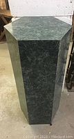 Full view of the green laminate hexagonal pedestal showing six sides and standing on a concrete floor.