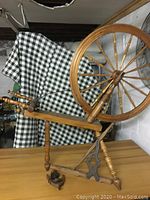 Full side view of the antique wooden spinning wheel showing the large wheel, frame and foot treadle.