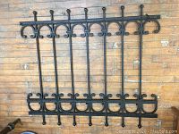 Full view of antique metal fence piece with ornamental scroll detailing, displayed against wooden floor background.