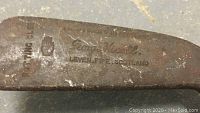 Close-up photo of putter head metal plate showing 'George Nicoll, Leven Fife Scotland' stamp indicating maker and origin.