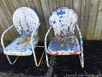 Two vintage metal patio chairs with heavily chipped and peeling white, red, and blue paint, showing rust and outdoor wear.