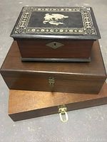 Three wood boxes stacked; top is decorative black with gold details, bottom two are plain wood with metal latches.