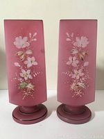 Front view of two pink rectangular Victorian glass vases with white floral decorations.
