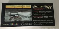 Front view of the Falcon VII remote control helicopter in its original black and clear packaging showing the toy through the transparent window and key features highlighted on the box.