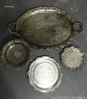 Overhead view of three silverplate trays including one large oval and two smaller round trays, showing overall condition and decoration.