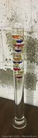 Full length image of the glass Galileo thermometer barometer showing cylindrical shape with colored glass spheres inside.