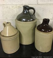 Three antique stoneware crocks grouped together against a wall, showing size difference and glaze details