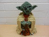 Front view of LEGO Yoda figure showing full body with arms holding a cane and detailed robe colors.