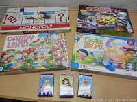 Top view of four board game boxes including Monopoly, Operation, Candy Land, and Chutes and Ladders plus three card games displayed on table.