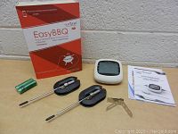 Photo showing the EasyBBQ box, two probes with caps, display unit, batteries, clamp, and user manual.