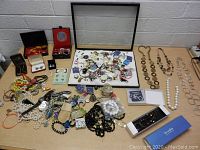 Wide view of table showing assorted jewelry including necklaces, bracelets, brooches, and jewelry display case with glass top.