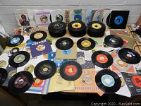 Overview of scattered and stacked vintage 45 RPM vinyl records with mixed sleeves on table.