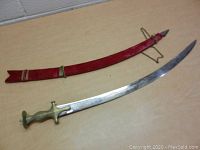 Curved sword with brass handle lying next to red sheath on a table.
