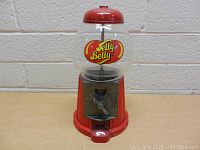 Front view of Jelly Belly candy dispenser showing the clear glass globe and red metal base with dispensing mechanism.