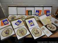 Nine Hummel collector plates from 1971-1979 in original boxes with certificates and booklets on table.