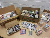 Wide overview of multiple boxes and stacks filled with assorted sports cards, including baseball, football, and basketball cards. Cards are loosely and neatly packed in boxes and stacks on table.