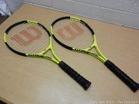 Pair of Wilson Titanium 3 tennis rackets lying flat on a surface, showing their yellow and black frames and red Wilson logos on the strings.
