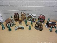 Porcelain Christmas village houses, trees, porcelain bridge and small figurines arranged on table against brick wall