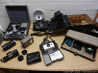 Wide view showing multiple vintage cameras, flash attachments, lenses, cases, and accessories on display surface.