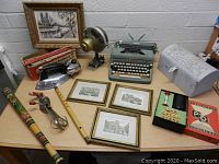 Assorted vintage items on a table including framed pictures, typewriter, iron with box, musical instruments, and decorative box
