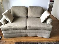 Front view of beige two-seater sofa with two throw pillows on hardwood floor