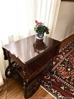Side view of tea wagon showing overall design, turned legs, lower shelf and large spoked wheels