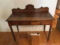 Front view of antique rustic console table showing decorative backboard, two drawers with knobs, and turned spindle legs.