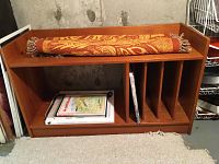 Wooden bookshelf/TV stand displaying dimensions and some books with rolled kilim rug on top.