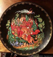 Collector plate showing a knight on horseback in front of a red castle with ornate towers and fairy tale elements on a black background with gold border
