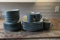 Stacks of 8 dinner plates, 8 salad plates, 8 bowls, 5 matching green mugs and one extra mug on countertop