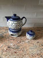 Blue and white folk design ceramic teapot on matching candle warmer, with sugar bowl showing same pattern and lid.