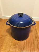 Blue stock pot with lid on wooden floor against white wall