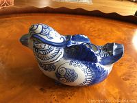 Photo of large blue and white porcelain bird figurine showing intricate feather details and curved tail on wooden surface