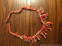 Red-orange Italian coral branch necklace laid on wood surface showing varied branch sizes