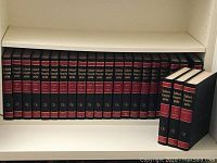 Complete Colliers Encyclopedia set with 24 volumes in black with red and gold spine detailing, arranged on a white shelf.
