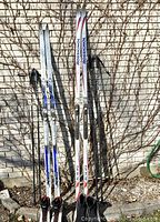 Two ski sets leaning against brick wall showing skis and poles