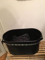 Black decorated woodbin with geometric design on side, containing dark folded fabric items inside.