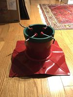 Christmas tree stand with red base and green interior, showing four tightening screws with red plastic handles.