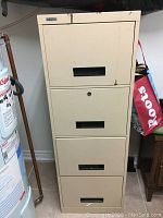 Full front view of the beige 4-drawer metal filing cabinet, showing wear and rust spots.