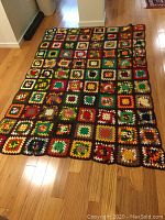Crochet bedspread laid flat on hardwood floor showing colorful granny square pattern