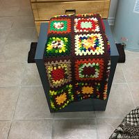 Multicolored handmade crochet bedspread draped over furniture, showing patchwork pattern with various colors.