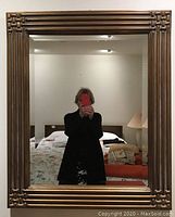 Front view of the large wall mirror showing its reflective glass surface and brown decorative frame with carved corner details.