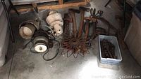 Wide view showing set of antique horns and assorted tools on concrete floor, including large metal spoked wheel horn and plastic tote with hand tools.