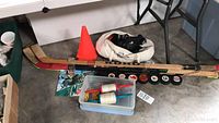 Photo showing the entire lot including two wooden hockey sticks, multiple hockey pucks, orange traffic cone, white bag, two kite string reels with white string, and a Mountain Dew signed on the floor.