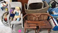 Full view showing white wicker child's rocker with two fabric dolls, wicker doll stroller with detached top, wooden child's table and chairs with detached table legs