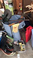 Photo showing garden lot items including rubber boots, gloves, electric hedge trimmer, sprayer wand, tools, and bin