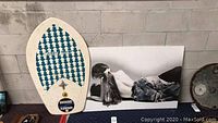 Photo showing Sherwood Aluminum 80 boogie board with blue arrow pattern and red strap next to black and white wall poster.