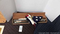 Folded American flag with flagpole sections in a box on the floor.