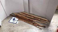 Seven rustic wooden walking sticks laid on the floor, showing various lengths and thicknesses.