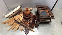 Full view of all items in the lot arranged on the floor showing picture frames, wooden vases, dried grass, feathers, carved faces, birch bark pieces, and round wooden items